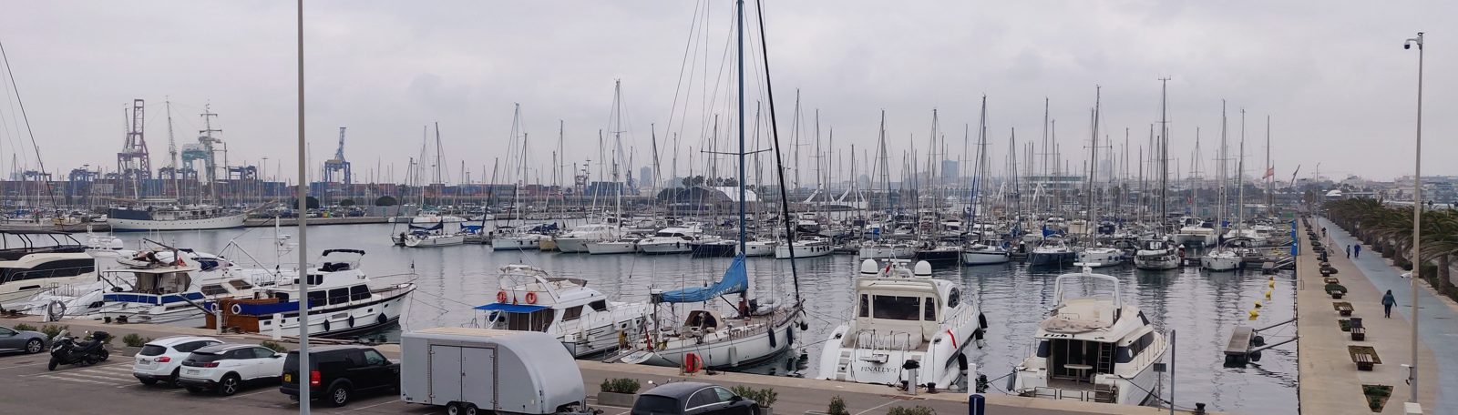 Barcos y veleros amarrados en La Marina de València, con las grúas del puerto al fondo